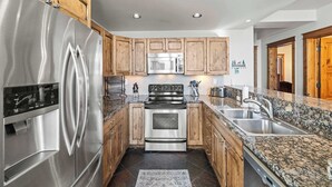 A modern kitchen with stainless steel appliances, wooden cabinets, granite countertops, and a built-in oven. - Black Bear Lodge #303 | Walk to West Wall Lift, Heated Garage + Hot Tub | 2BR (Crested Butte)