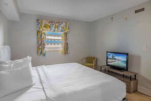 Ein Hotelzimmer mit Bett, Fernseher auf einem Holztisch, einem Sessel und einem Fenster mit Vorhängen.