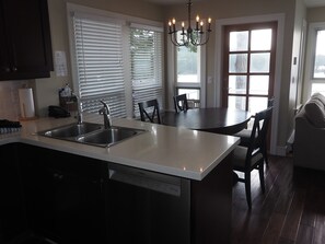 A kitchen with a dishwasher, double sink, and a dining area with a round table and chairs. - Cosy 2 bedroom with expansive Ocean view and massive deck (Otter Bay)