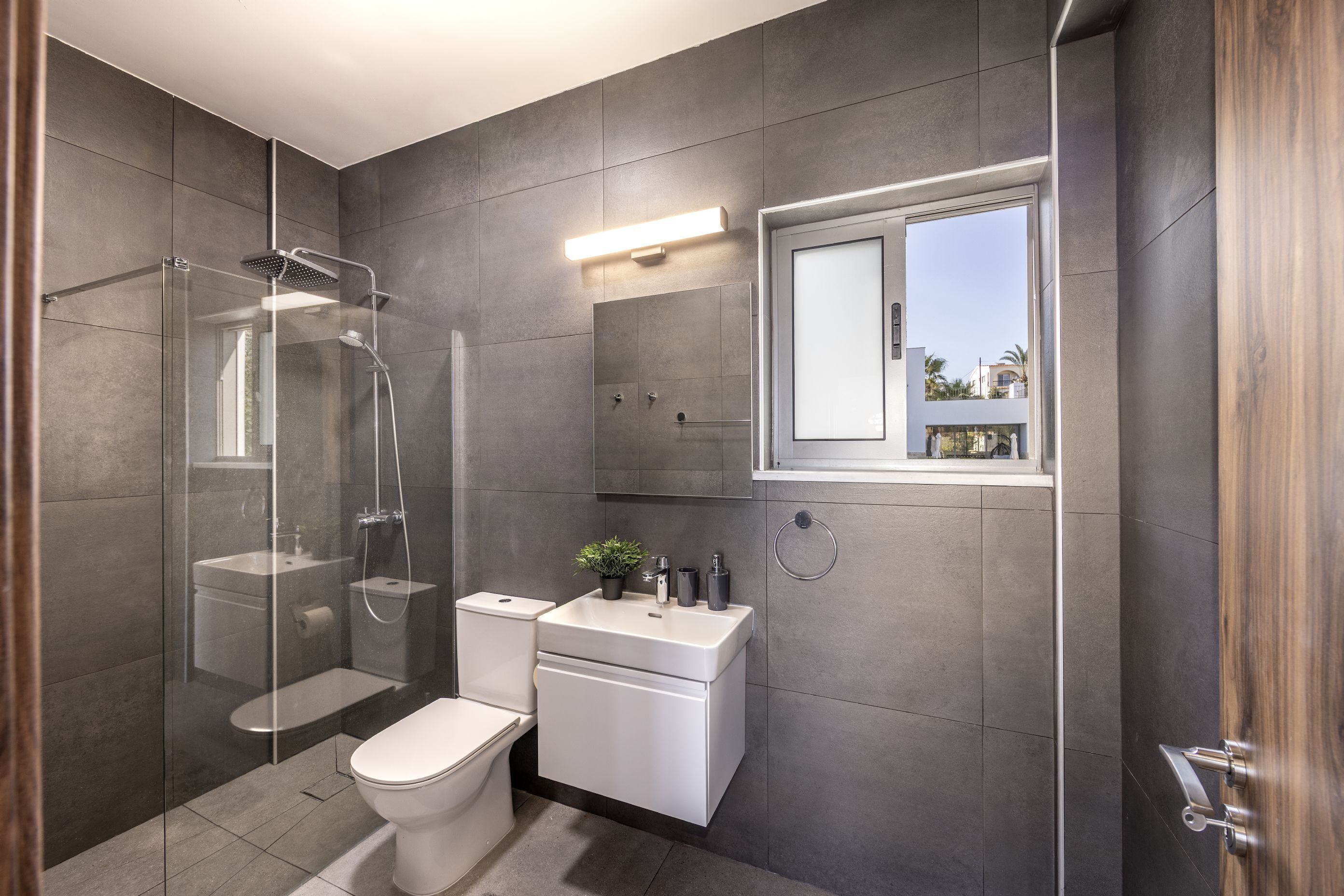 A modern bathroom with a glass-enclosed shower, a toilet, a sink, and a window with a view of the outside.