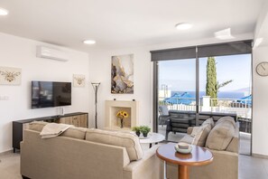 Ein modernes Wohnzimmer mit einer Couch, Fernseher, Kamin und einem Balkon mit Gartenmöbeln.