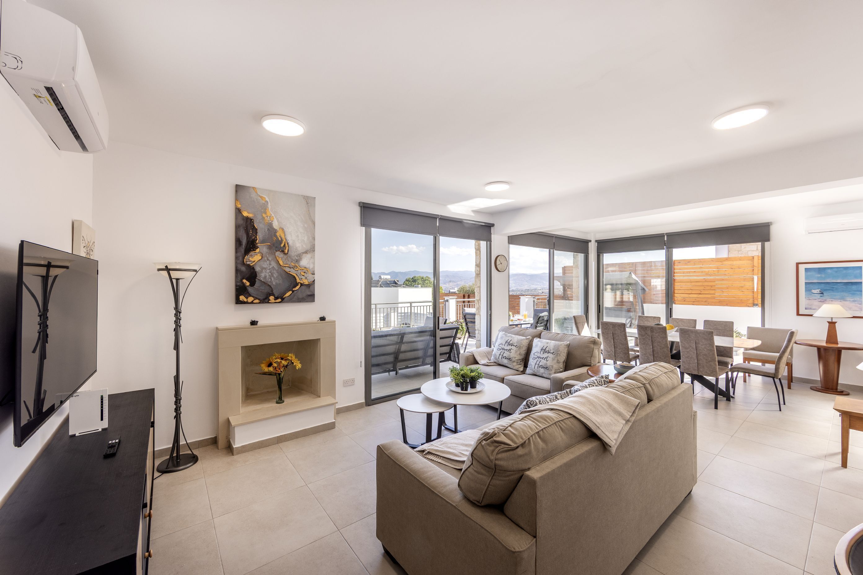 Un saló modern amb un sofà, una taula de centre i una televisió. Hi ha una llar de foc amb un ram de flors. L'habitació té grans finestres i un balcó.