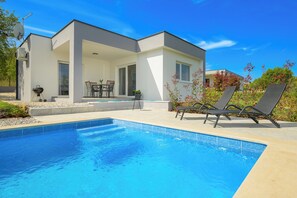Une maison moderne dotée d’une piscine, de mobilier d’extérieur et d’une antenne parabolique.