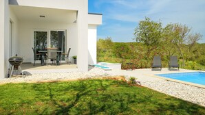 A modern house with a patio, outdoor seating, a barbecue, and a swimming pool.