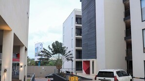 Un bâtiment moderne avec une façade blanche, un mur d’accent rouge et un SUV blanc garé devant.