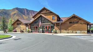 A wooden lodge with a large entrance, a flag, and a mountain backdrop.