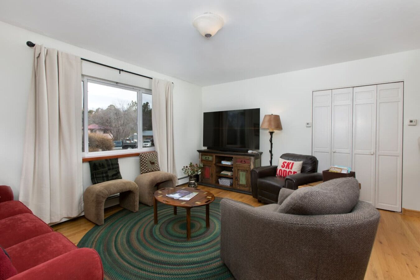 A modern living room with a flat-screen TV, leather sofas, a coffee table, and a view of the outdoors through a large window.