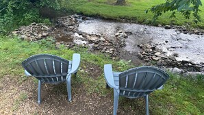 Twee stoelen gericht op een beek met rotsen en groen op de achtergrond.