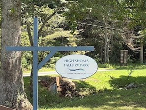 Señal de High Shoals Falls RV Park con una carretera despejada que conduce al parque.