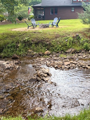 Ein Bach mit Steinen, eine Holzterrasse und Adirondack-Stühle.