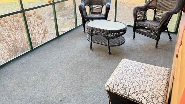 Een kamer met een groot raam, twee rieten stoelen, een klein rond tafeltje en een kamerkleed met dessin.