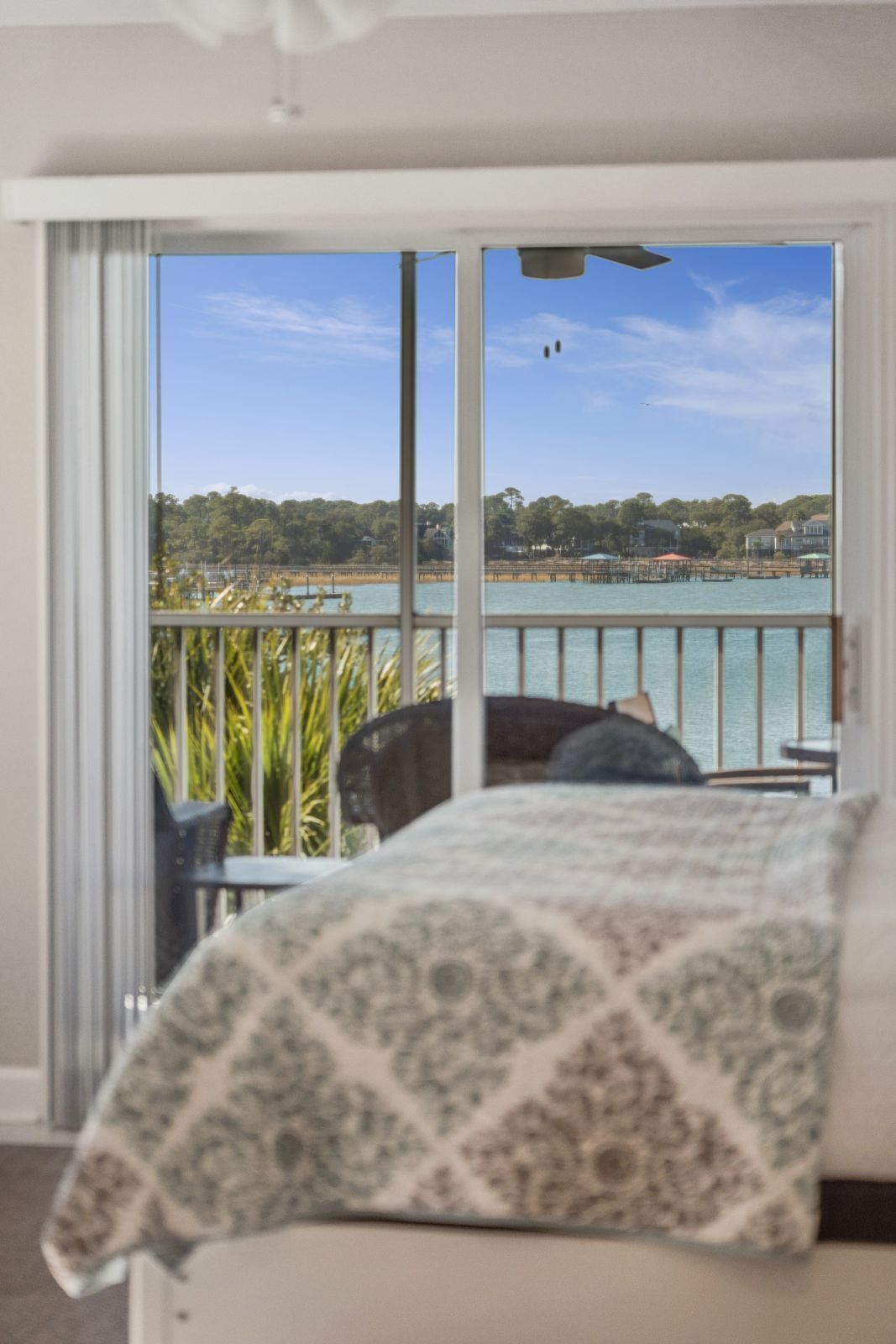 Ein Schlafzimmer mit einer großen Schiebeglastür, die auf einen Balkon mit Blick auf ein Gewässer und eine Anlegestelle führt.