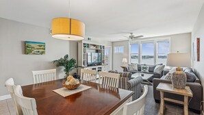 En moderne stue med et træspisebord, hvide stole, en sofa og et fjernsyn.