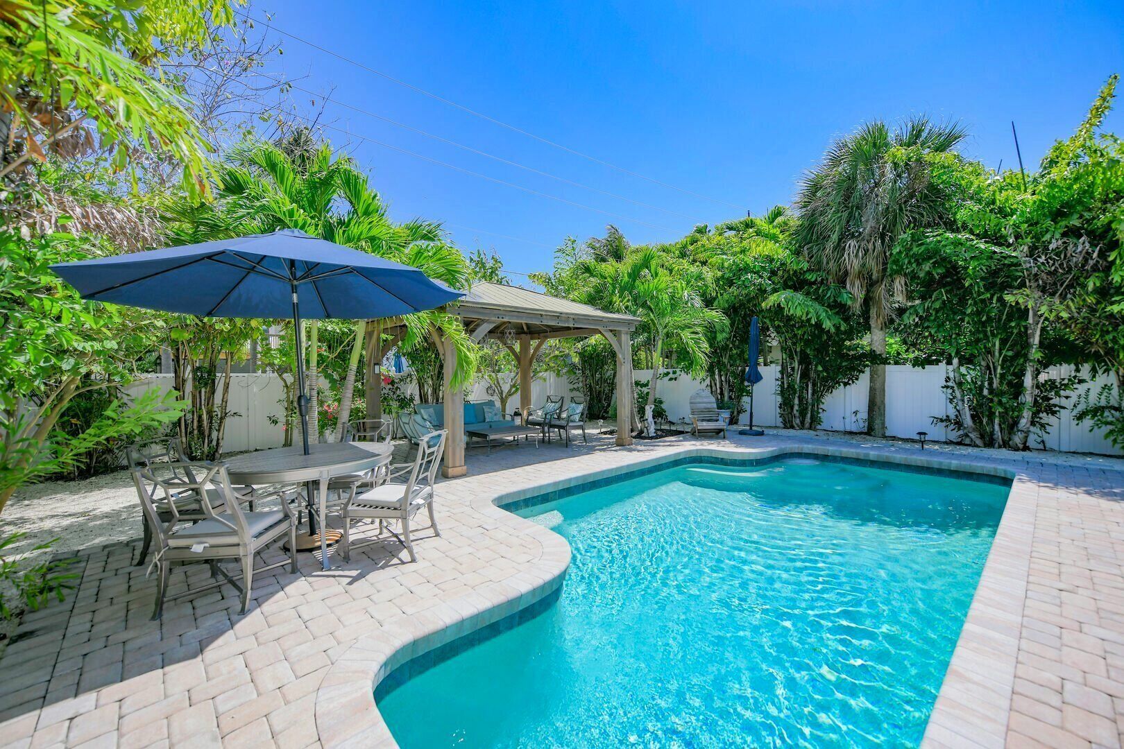 A swimming pool with a curved edge, surrounded by a patio area with a table and chairs, and a covered seating area.