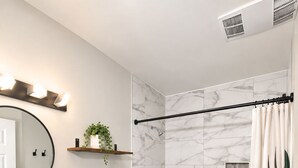 Une salle de bain avec une douche en marbre, des toilettes blanches, un meuble-lavabo en bois avec un vasque et un miroir.