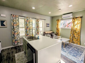 Una cocina compacta con una isla central, lavavajillas integrado y una zona de comedor con una mesa y sillas pequeñas.