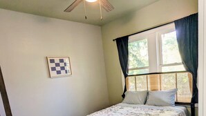 Ein Schlafzimmer mit Bett, Deckenventilator, Fenster mit Vorhängen, Heizkörper und Tür.