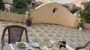 A dining table with plates of food, a chair, and a view of pyramids in the background. - Timo Pyramids View : Deluxe Triple Room (Giza Governorate)