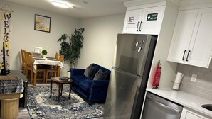 Ett modernt kök med ett kylskåp i rostfritt stål, vita skåp och en matplats med en blå soffa och ett matbord i trä.