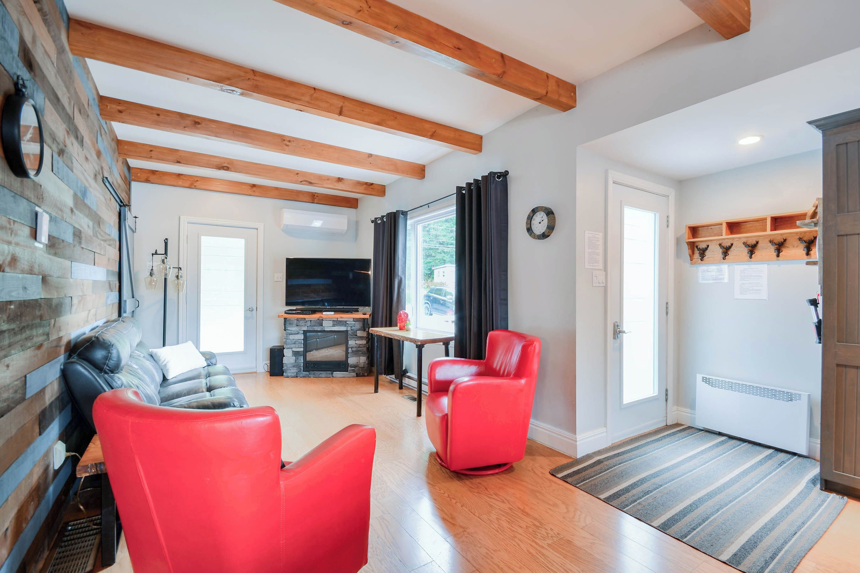A living room with a fireplace, red chairs, a sofa, and a wooden ceiling.