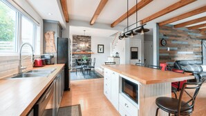 Une cuisine moderne avec des poutres en bois, une cheminée en pierre et un coin repas offrant une vue sur l’extérieur.