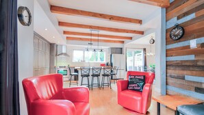 Une cuisine moderne avec des poutres en bois, un coin repas avec des chaises rouges et un mur en bois orné d’une horloge.