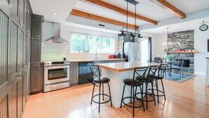 Une cuisine moderne avec des poutres en bois, un grand îlot central doté de tabourets, des appareils électroménagers en acier inoxydable et une cheminée en pierre.