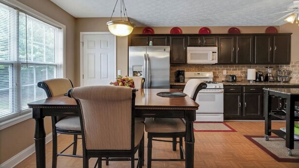 A kitchen with a dining table, chairs, a refrigerator, microwave, and a stove. - 6BR Home • Spacious Yard + Grill • Peaceful Suburb (Locust Grove)