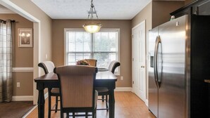 A dining area with a table and chairs, a chandelier, and a refrigerator. - 6BR Home • Spacious Yard + Grill • Peaceful Suburb (Locust Grove)