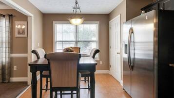 A dining area with a table and chairs, a chandelier, and a refrigerator.
