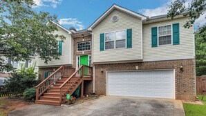 A two-story house with a front entrance, a staircase, and a garage. - 6BR Home • Spacious Yard + Grill • Peaceful Suburb (Locust Grove)