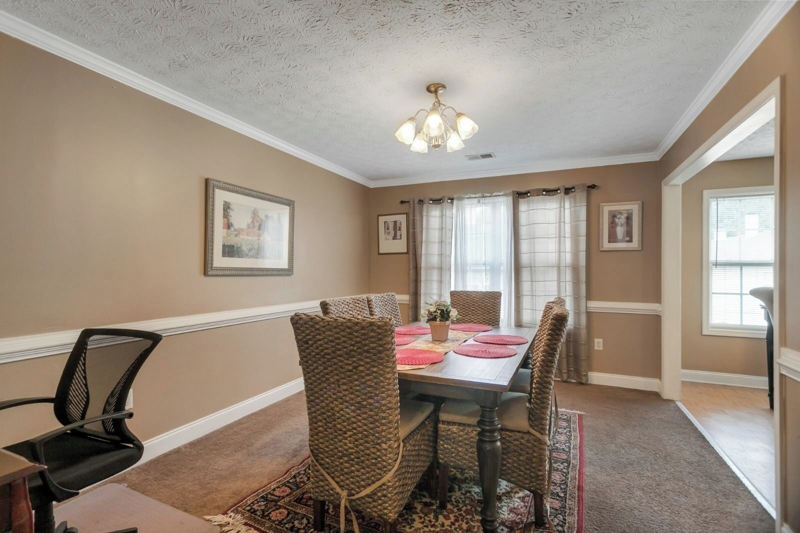 A dining room with a wooden table, woven chairs, and a chandelier.