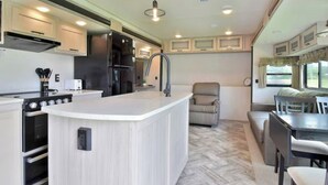 Een compacte keuken met een centraal eiland, geïntegreerde apparatuur en een eethoek met een tafel en stoelen.