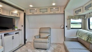 Een compact camperinterieur met een kitchenette, een zachte zithoek en een raam met uitzicht op de natuur.