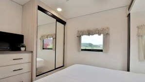 Een slaapkamer met een bed, een tv op een dressoir, een raam met gordijnen en een schuifdeur.