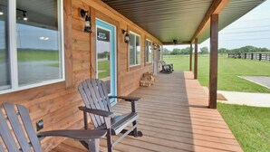 Een houten hutje met een overdekte veranda, twee Adirondack stoelen en uitzicht op een groen veld.