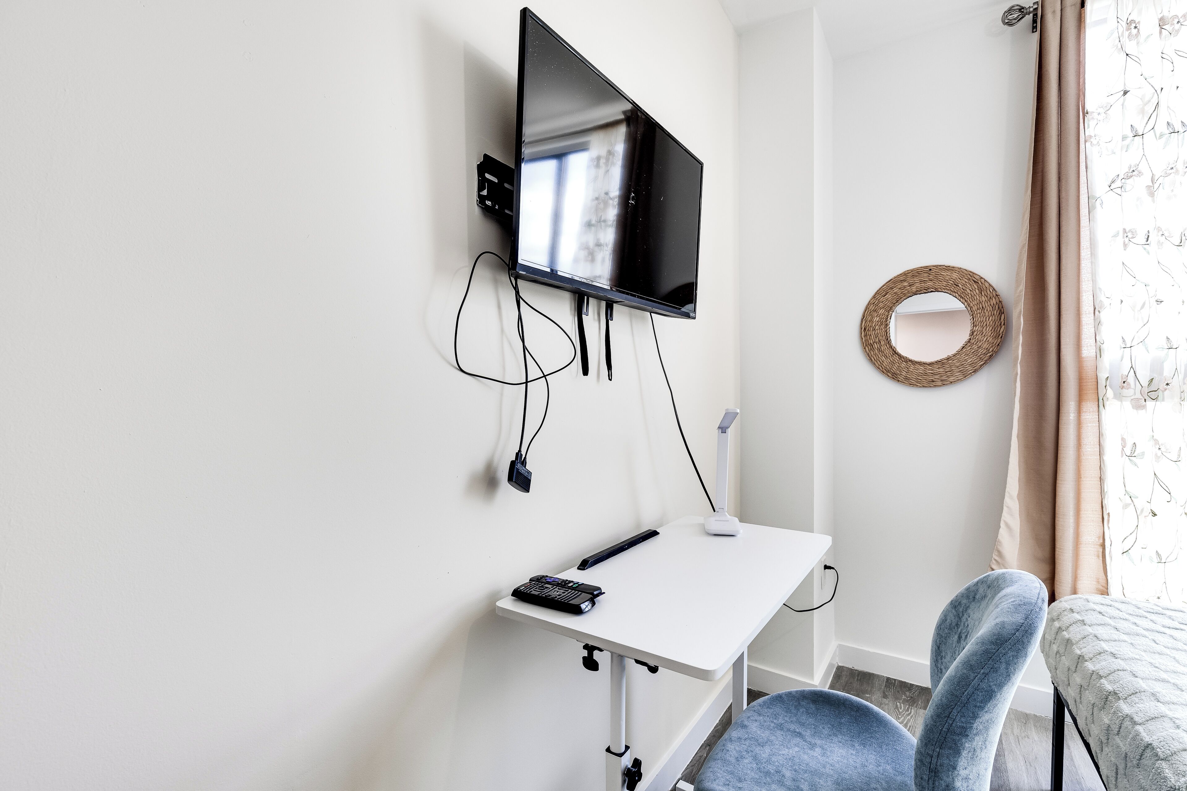 A room with a mounted TV, a desk with a keyboard and mouse, a chair, and a decorative mirror on the wall.