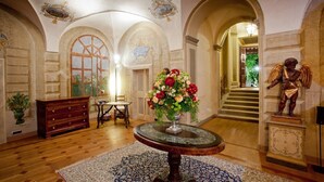 Un passadís majestuós amb sostres arquejats, una taula rodona amb un centre floral, i una estàtua d'un àngel.