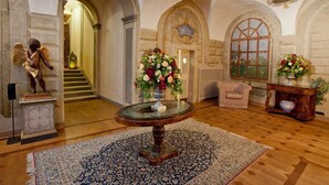 Ein prachtvoller Saal mit einer Marmortreppe, einem runden Tisch mit Blumenvase und einer Engelsstatue.