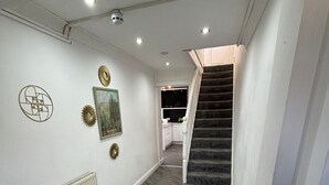 Un corridoio con pavimento a spina di pesce, pareti bianche e una scala che conduce a un angolo cottura.