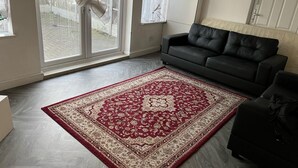 Un soggiorno con un tappeto grande a motivi rosso e beige, un divano in pelle nera e un frigorifero bianco.