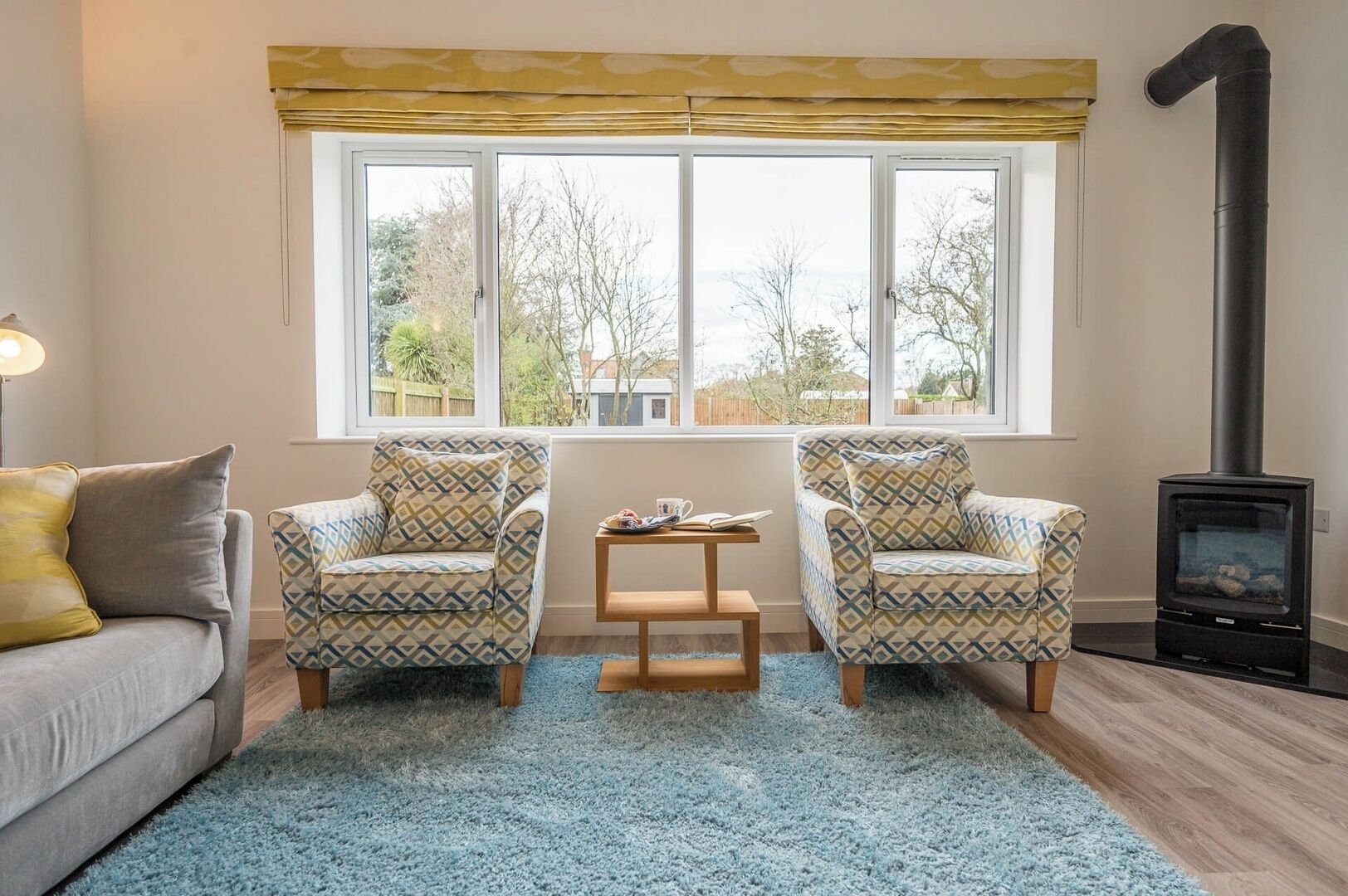 Una sala de estar acogedora con un sofá, dos sillones estampados, una pequeña mesa de madera y un estufa de leña negra.