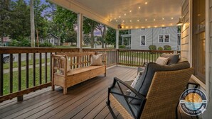 Une véranda couverte avec un plancher en bois, un banc, une chaise et des guirlandes lumineuses.