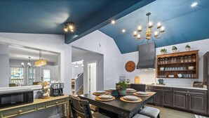 Une cuisine moderne avec un coin repas, comprenant un grand îlot central, des meubles de rangement aux couleurs sombres et un plafond bleu.