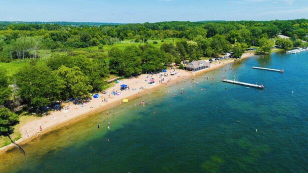 Vue aérienne d’une plage avec une eau cristalline, un rivage sablonneux et une zone boisée en arrière-plan.