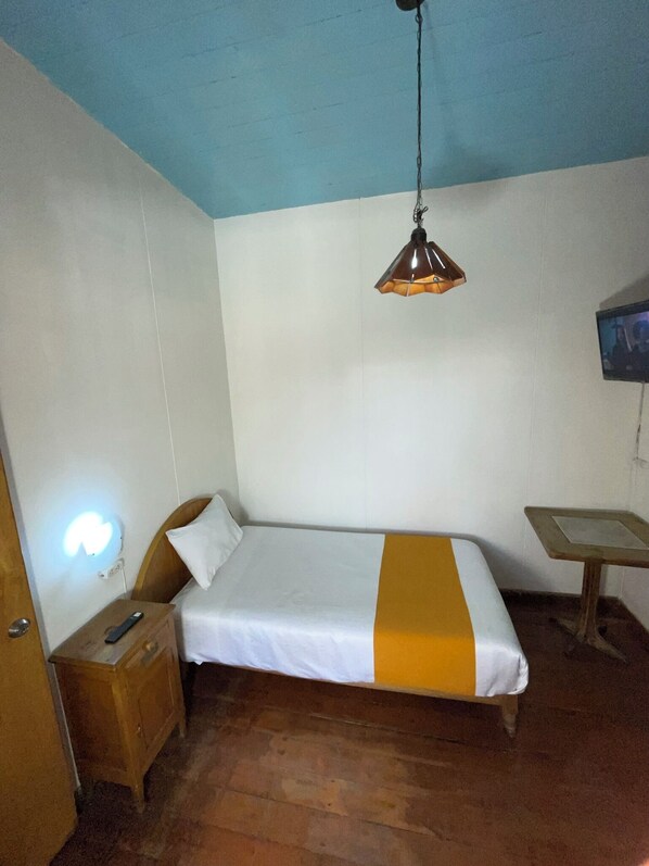 A small, single-bed room with a wooden nightstand, a bedside table, a hanging lamp, and a television on the wall. - HOSTAL LLUVIA DE ORO 3 min from the historic center of Arequipa's main square. (Arequipa)