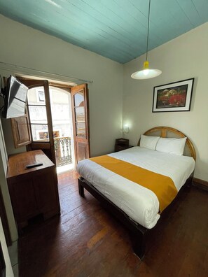 A bedroom with a wooden bed, a bedside table, a hanging light fixture, and a door leading to an outdoor area. - HOSTAL LLUVIA DE ORO 3 min from the historic center of Arequipa's main square. (Arequipa)