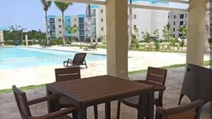 Un patio exterior con una mesa y sillas, con vistas a una piscina y un edificio con balcones.