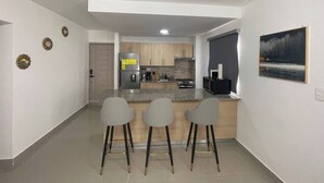 Una cocina moderna con una isla central, tres taburetes de bar y un cuadro en la pared.