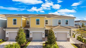 A row of two-story townhouses with attached garages, a clear blue sky, and well-maintained landscaping. - The Serenity Townhome (Kissimmee)